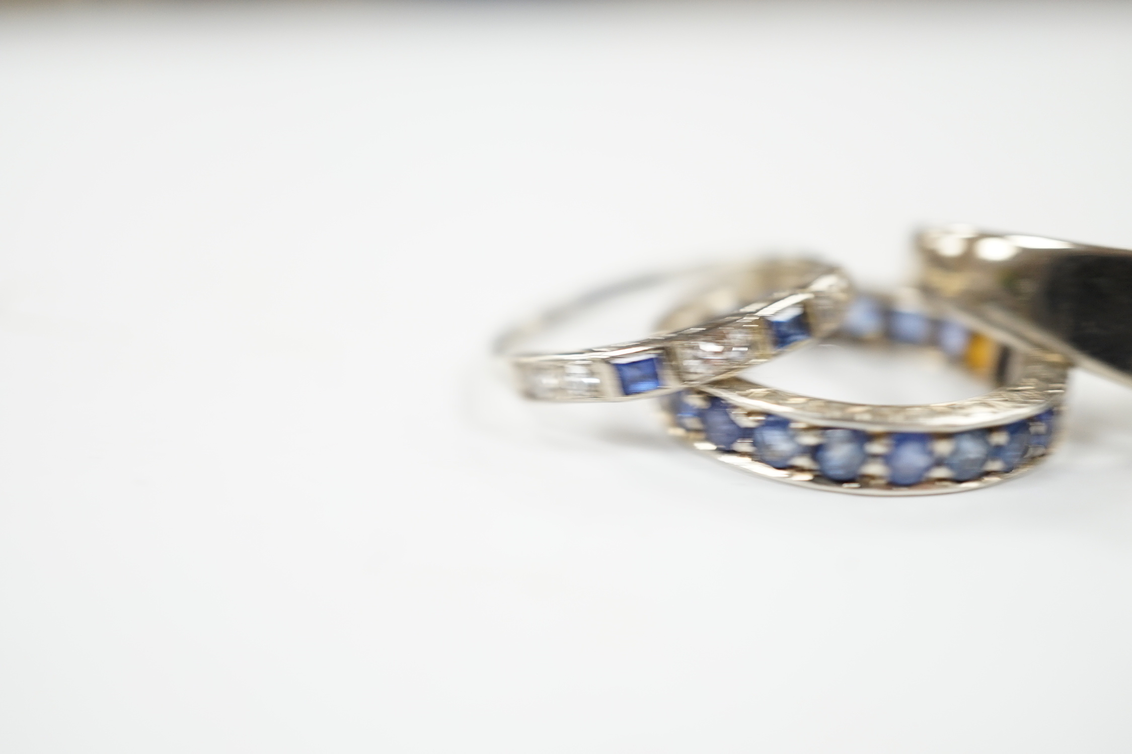 An 18k white metal, emerald and diamond set dress ring, size O, a white metal and sapphire set full eternity ring (stones missing) and an 18ct, sapphire and diamond set half hoop ring, gross weight 10 grams.